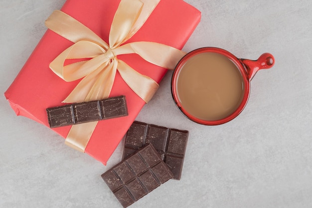 Taza de café, chocolate y caja de regalo sobre superficie de mármol