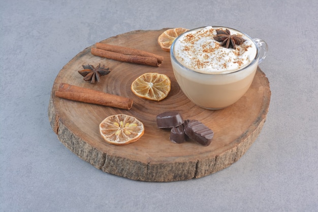 Una taza de café cremoso y canela en rama sobre tablero de madera.