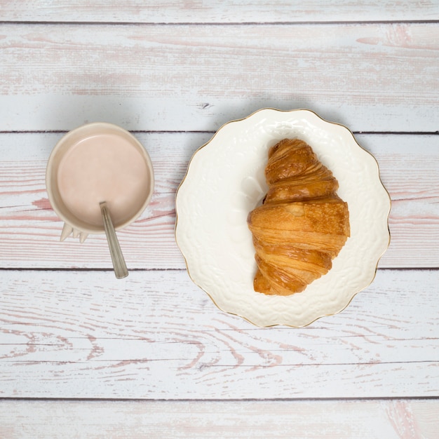 Taza de café y croissant en plato de cerámica sobre mesa de madera