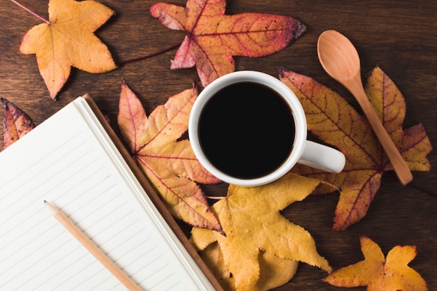 Taza de café y cuaderno sobre fondo de hojas de otoño