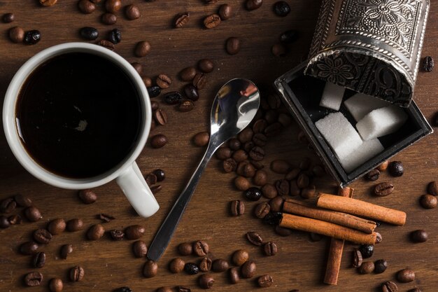 Taza de café con una cuchara cerca de una caja de azúcar y canela