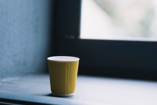 Taza de café desechable amarilla cerca del alféizar de la ventana