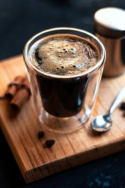 Taza de café espresso doble con palitos de canela y granos de café sobre una tabla de madera