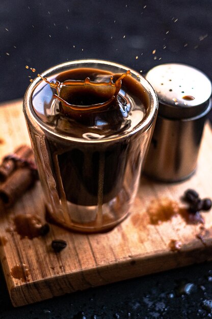 Taza de café espresso doble con palitos de canela y granos de café sobre una tabla de madera