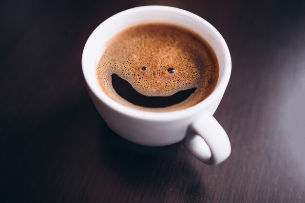 Taza de café con espuma, cara de sonrisa, en el escritorio aislado
