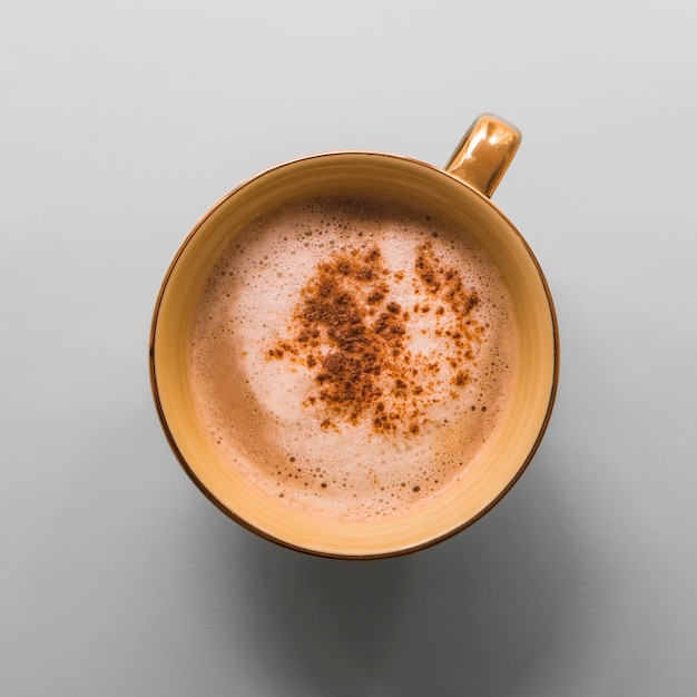 Taza de café con espuma de leche y cacao en polvo sobre fondo gris