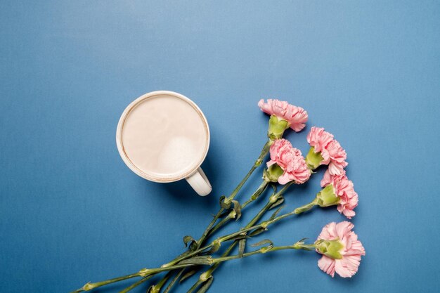 Taza con café y flores de clavel rosa en la mesa azul Vista superior espacio plano para texto