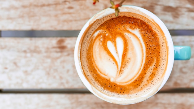 Taza de café con forma de corazón arte latte en mesa de madera