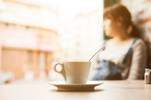 Taza de café frente a la mujer desenfoque que mira lejos