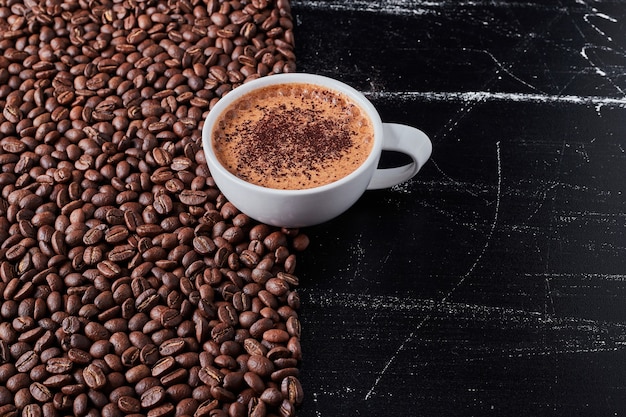 Taza de café con frijoles alrededor.