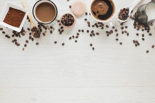 Taza de café; frijoles asados frijoles crudos Café en polvo y leche en mesa de madera blanca