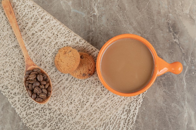 Taza de café, galletas en la superficie de mármol con granos de café.