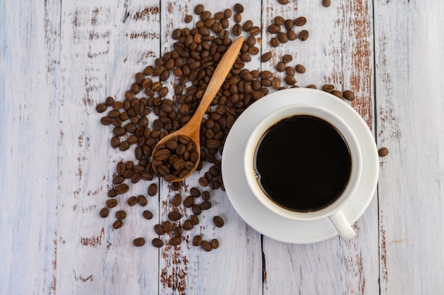 Taza de café y granos de café en la cuchara de madera sobre la mesa blanca.