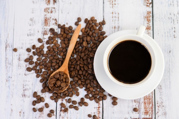 Taza de café y granos de café en la cuchara de madera sobre la mesa blanca.