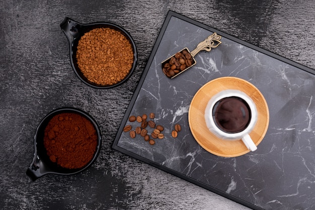 Una taza de café con granos de café en una cuchara de metal sobre una superficie oscura