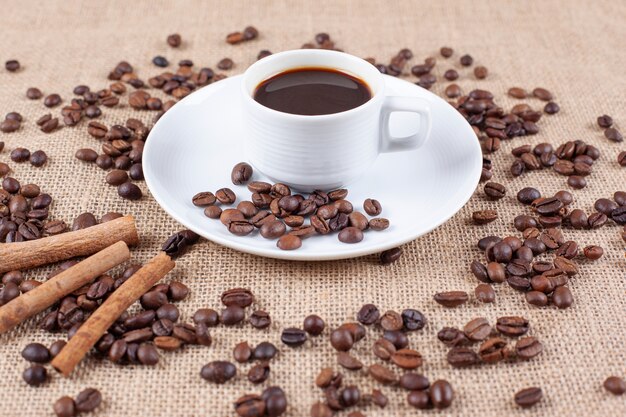 Una taza de café con granos de café y ramitas de canela.