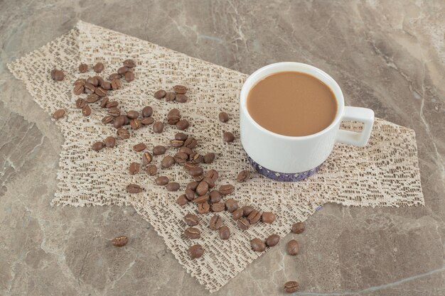 Taza de café y granos de café en la superficie de mármol con arpillera