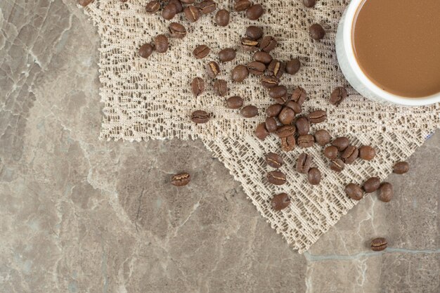 Taza de café y granos de café en la superficie de mármol con arpillera