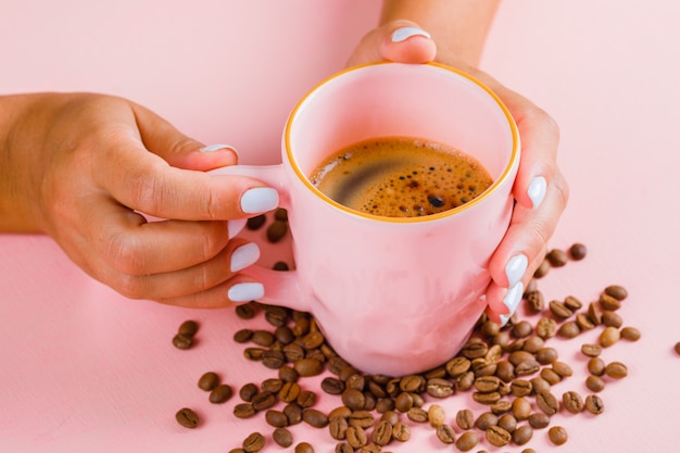 Taza de café y granos de café en superficie rosa