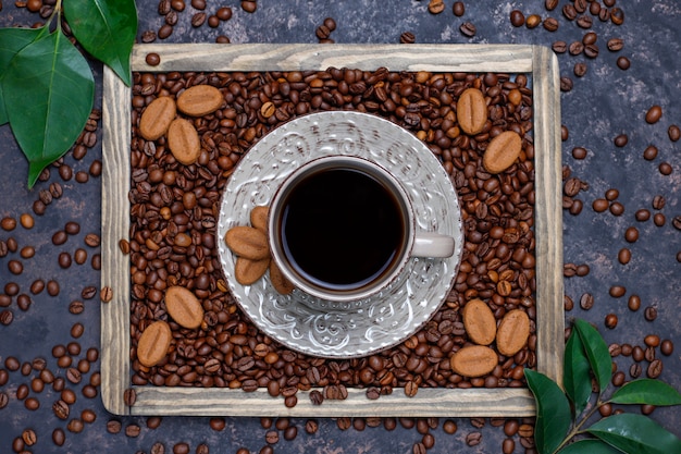 Una taza de café con granos de café tostados y galletas con forma de grano de café sobre una superficie oscura