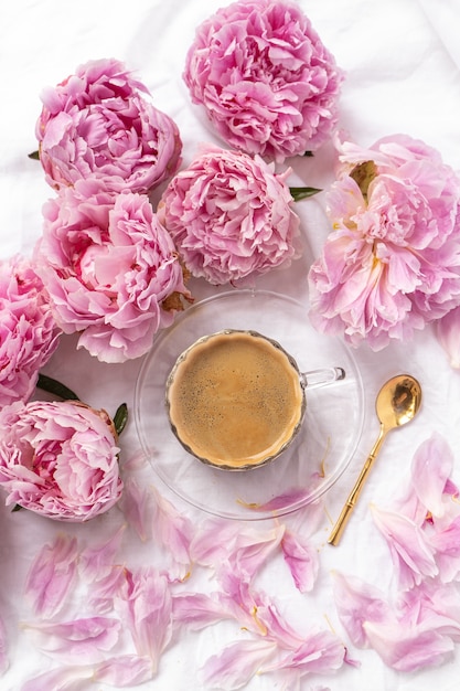 Foto gratuita taza de café instantáneo en la mesa con peonías rosas bajo las luces