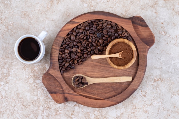 Una taza de café junto a una bandeja de granos de café y polvo de café molido