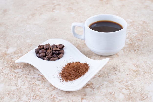 Una taza de café junto a los granos de café y el polvo de café molido en un plato elegante