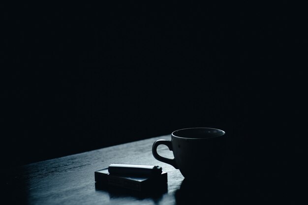 Taza de café junto a un paquete de cigarrillos y un encendedor