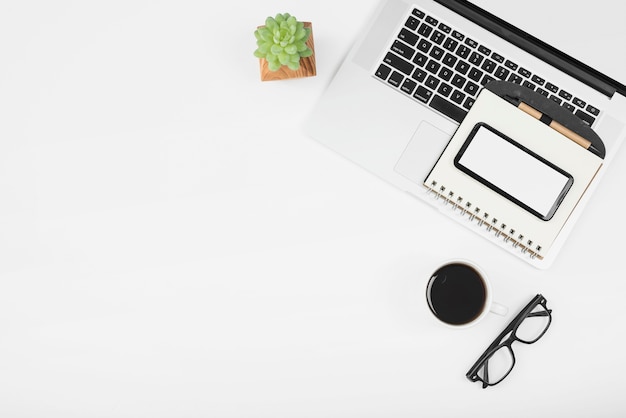 Foto gratuita taza de café con laptop; teléfono celular y diario con pluma sobre fondo blanco