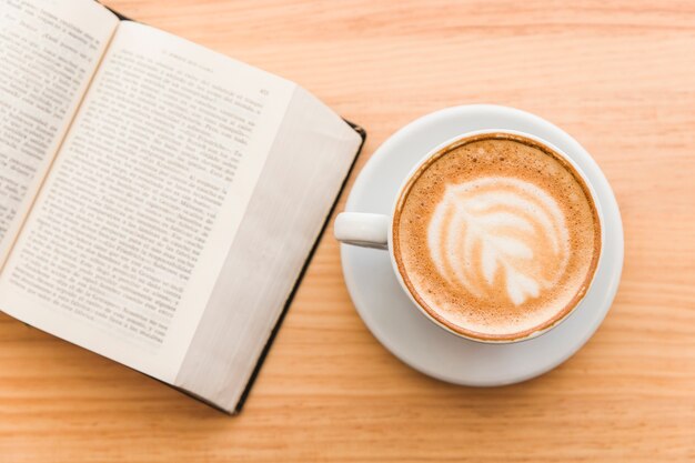 Taza de café con leche del arte en un café del capuchino y un libro abierto en la tabla