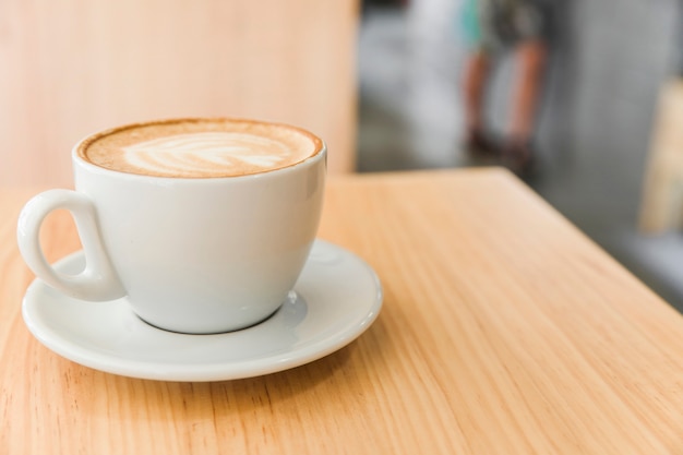 Taza de café con leche del arte en un café del capuchino en la tabla de madera