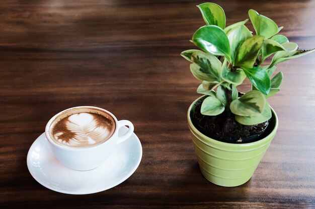 Taza de café con leche caliente con olla pequeña decoración árbol verde