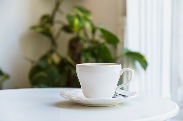 Taza de café con leche y una cuchara en el plato de cerámica sobre mesa blanca