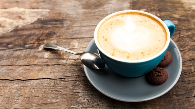 Taza de café con leche con deliciosas galletas en el escritorio de madera