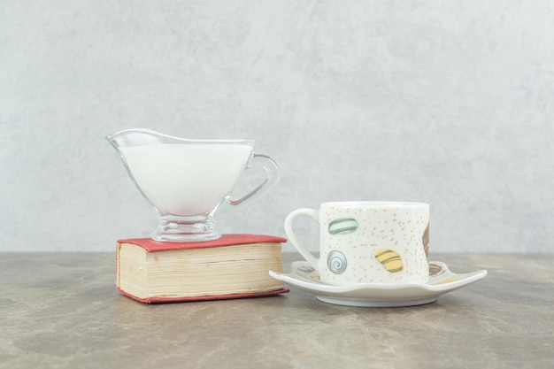 Taza de café con leche y libro sobre mesa de mármol.