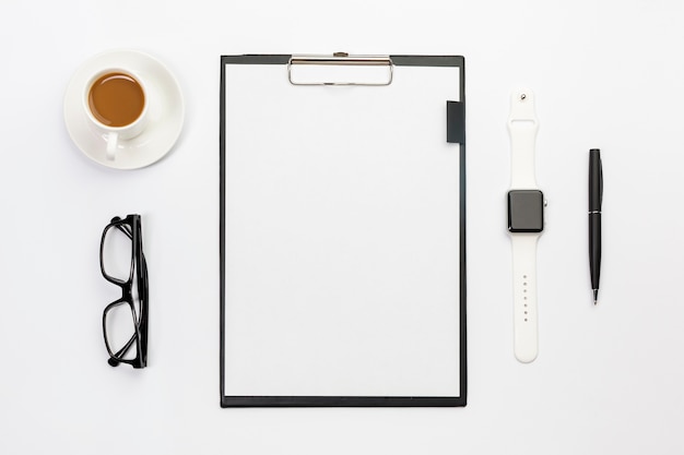 Foto gratuita taza de café, lentes, reloj inteligente, bolígrafo y portapapeles de papel en blanco en el escritorio blanco