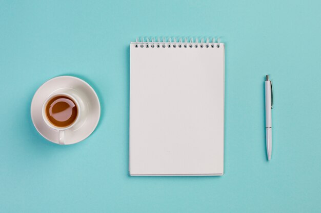 Taza de café, libreta espiral en blanco y pluma en el escritorio de oficina azul