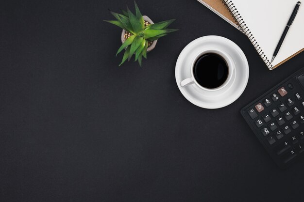 Una taza de café, libretas, una calculadora en una vista superior de fondo negro