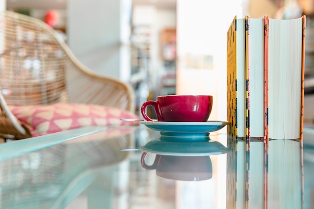 Foto gratuita taza de café y libro cerrado en la mesa de vidrio reflectante