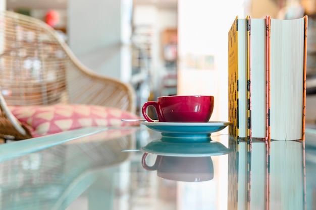 Taza de café y libro cerrado en la mesa de vidrio reflectante