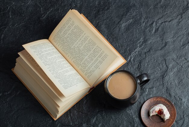 Una taza de café con libro sobre una superficie oscura.