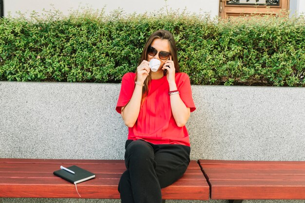 Taza de café de moda de la mujer que habla en el teléfono móvil