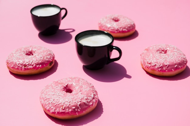 Taza de café negro con donuts sobre fondo rosa