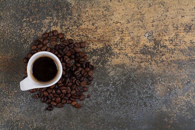 Taza de café negro con granos de café sobre la superficie de mármol.