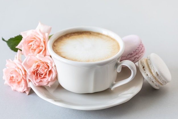 Taza de café, pasta para el pastel y rosas rosadas sobre una superficie gris. Copie el espacio.