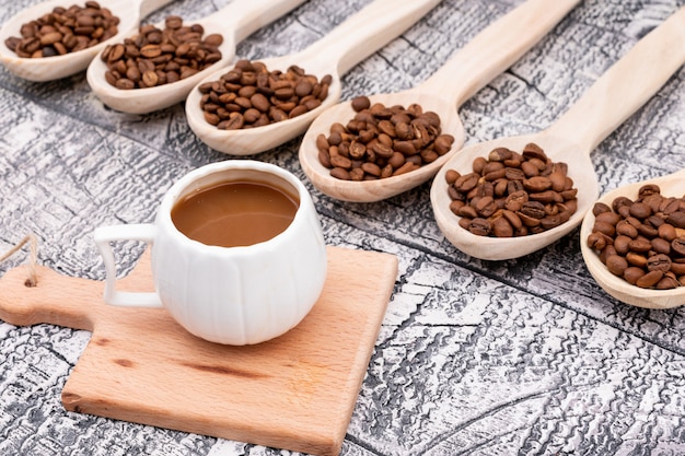 taza de café en una pequeña tabla de madera granos de café en una cuchara de madera sobre una superficie de madera