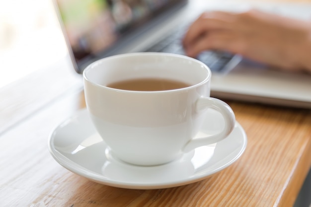 Taza de café con una persona trabajando en un portátil al lado