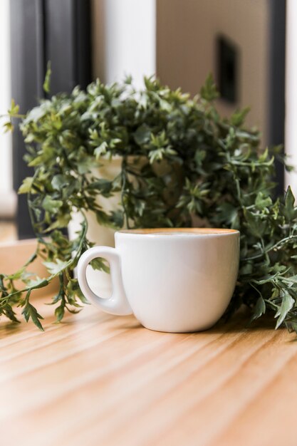 Taza de café con planta en maceta en la superficie de madera