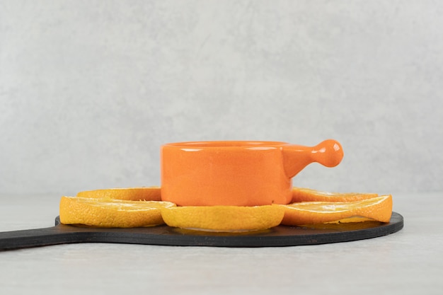 Taza de café y plato de rodajas de naranja en tablero oscuro