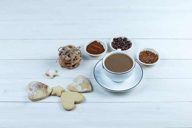 Taza de café de primer plano con granos de café, café instantáneo, cacao, diferentes tipos de galletas sobre fondo de tablero de madera blanca. horizontal